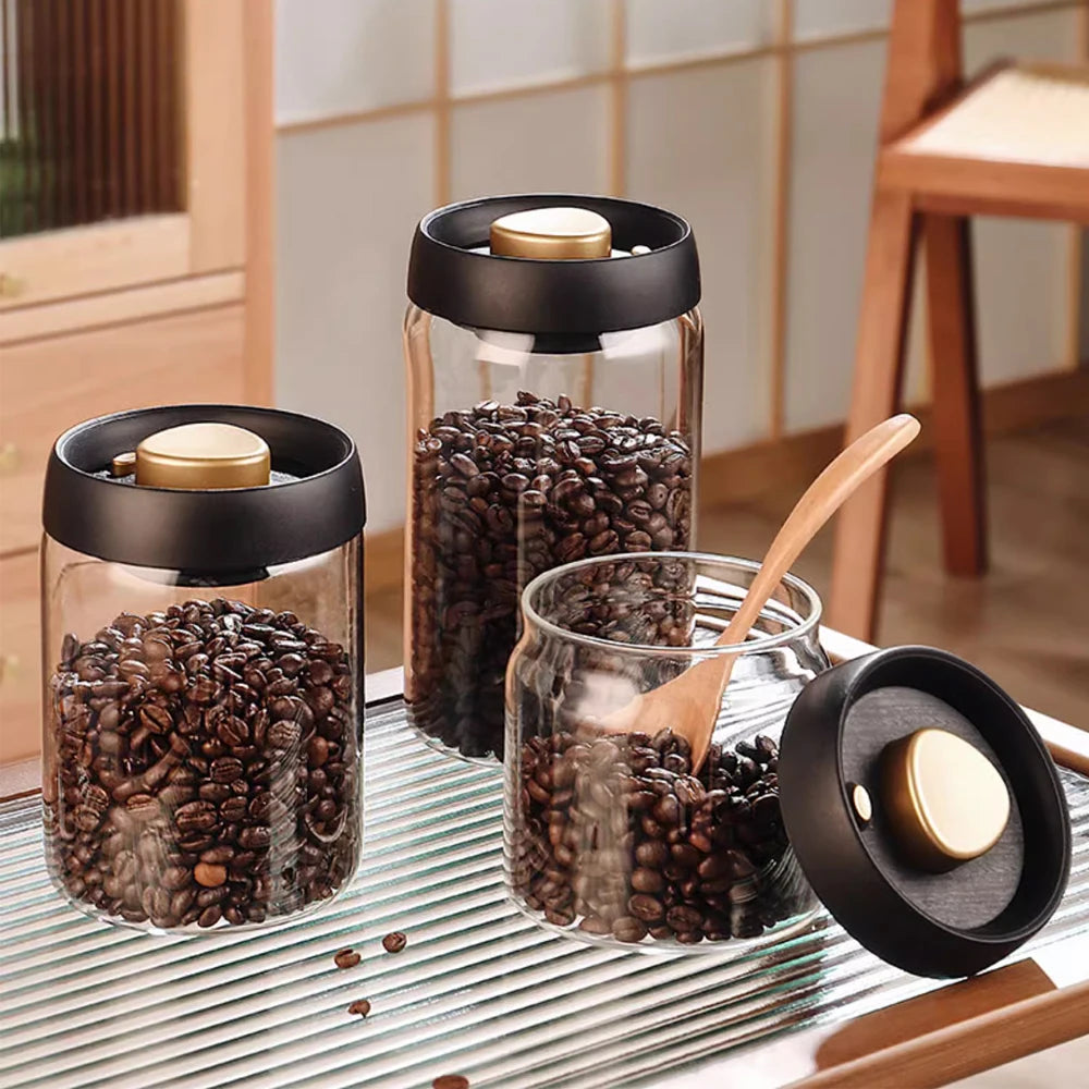 Three glass jars with coffee beans and black lids on a kitchen counter.